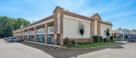 A multi-story hotel with a parking lot and a landscaped area with small trees and shrubs.