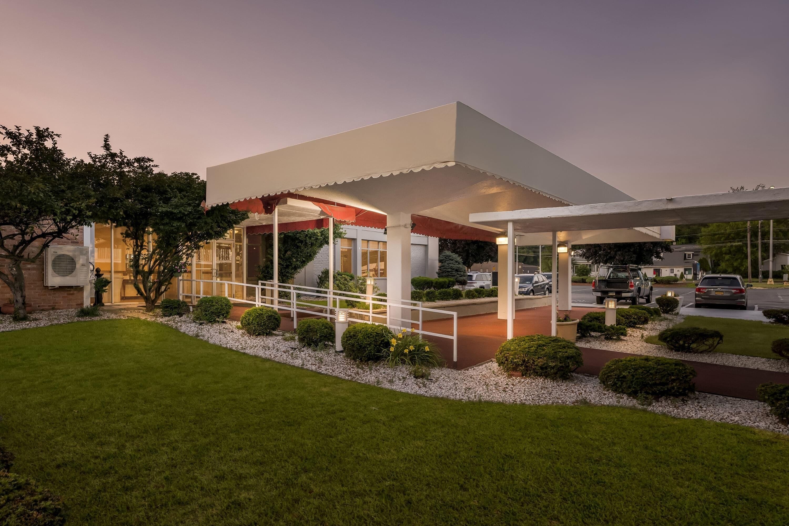 A modern building with a covered outdoor area, a paved walkway, and a parking lot.