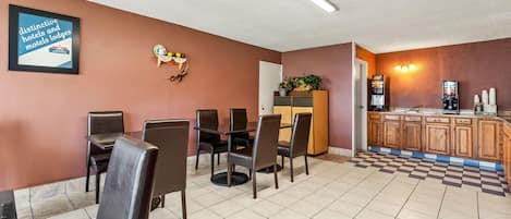 Un comedor con mesa y sillas, una zona de cocina con cafetera y un letrero en la pared.