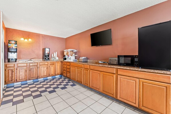 A kitchen with wooden cabinets, a microwave, a coffee maker, and a flat-screen TV. - Howard Johnson by Wyndham Albany (Albany)