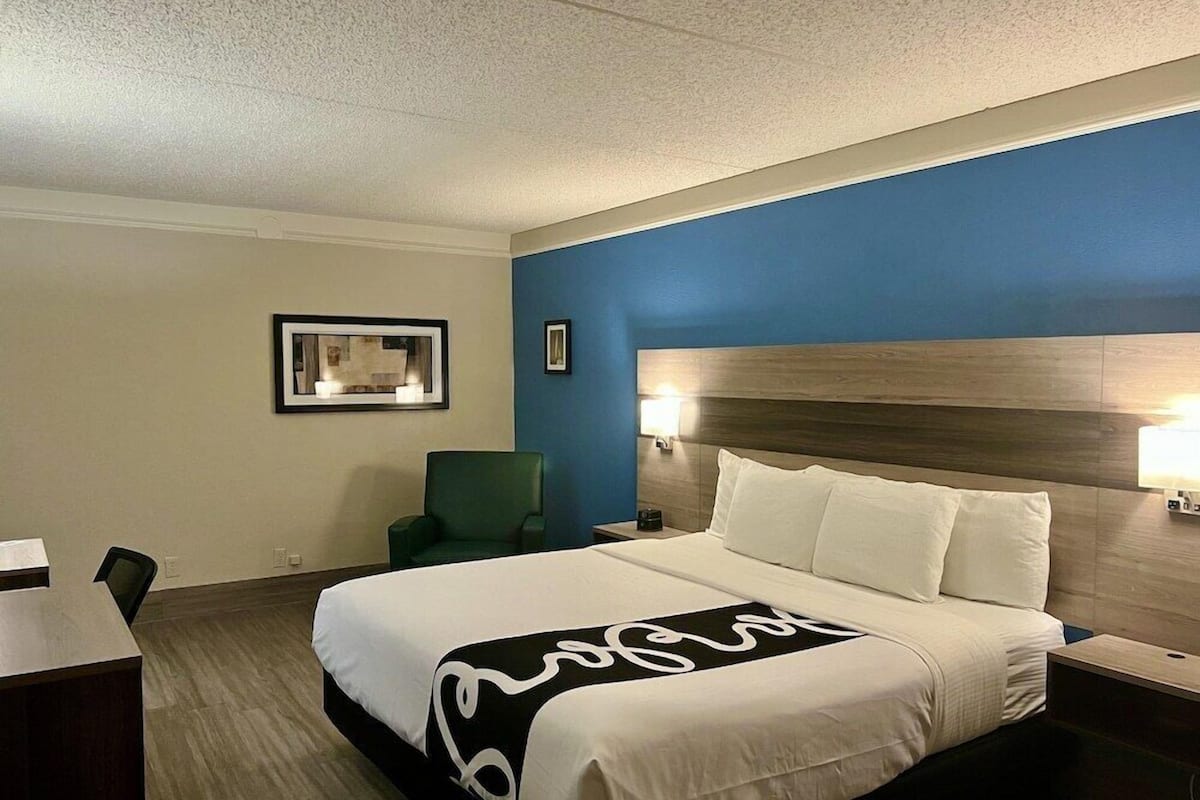 Quarto de hotel com cama, escrivaninha, cadeira e mesa de cabeceira.