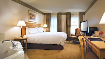 Habitación de hotel con cama, escritorio, silla, televisor y baño con lavamanos y bañera.