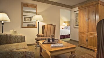 Habitación de hotel con sofá, sillón, aparador de madera y cama con cabecero.