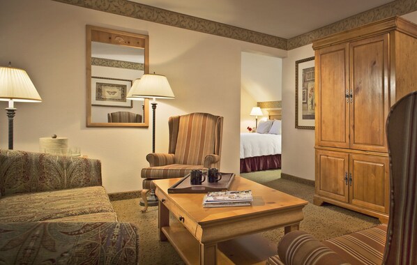 A hotel room with a sofa, armchair, wooden cabinet, and a bed with a headboard. - Inn on the Square (Falmouth)