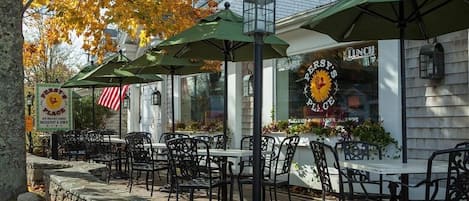 Outdoor seating with tables and chairs, covered by green umbrellas, and a sign for a breakfast and lunch place.