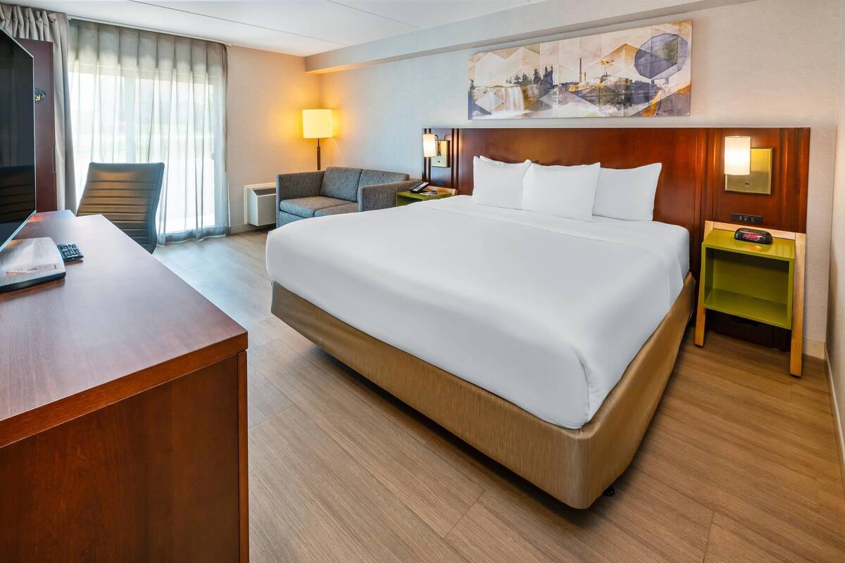A hotel room with a large bed, a desk, a chair, a lamp, and a painting on the wall.