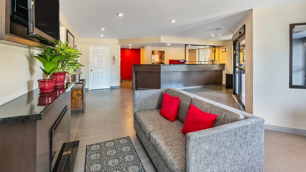 A modern living area with a grey sofa, red cushions, a kitchen area with a TV, and a red accent wall. - Comfort Inn Sudbury City (Sudbury)