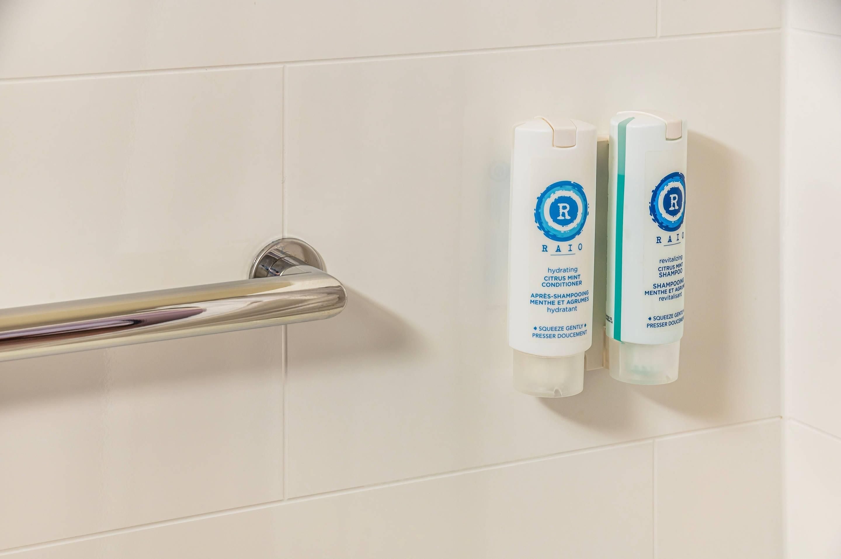 Due flaconi di articoli da bagno con un logo e una scritta blu su un muro rivestito di piastrelle bianche.