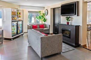 Una sala de estar moderna con un sofá gris, cojines rojos, un televisor de pantalla plana, chimenea y un mini refrigerador lleno de aperitivos.