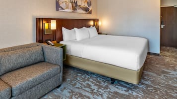 A hotel room with a large bed, a sofa, a nightstand, and a painting on the wall.