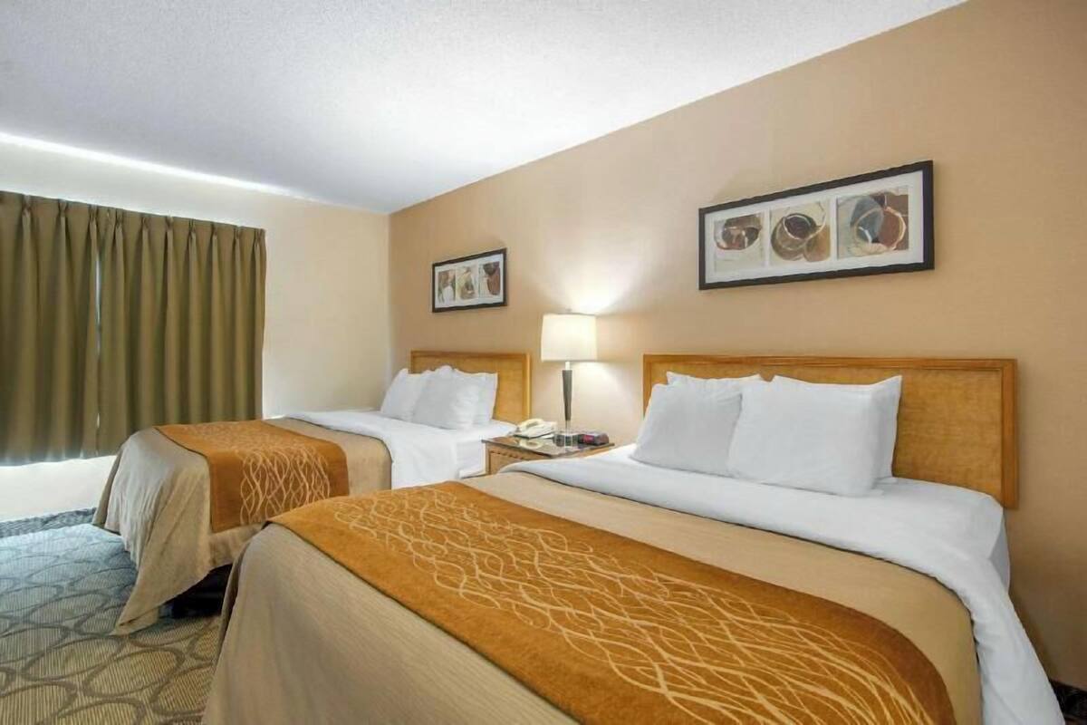 A hotel room with two beds, a nightstand with a lamp, and a window with curtains.