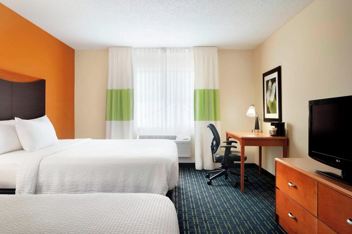 A hotel room with two beds, a desk with a TV, and a chair.