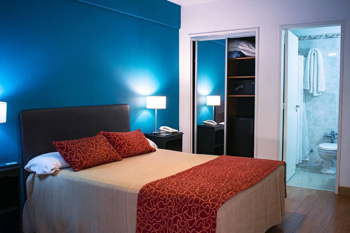 A hotel room with a bed, bedside lamps, a telephone, a wardrobe, and a bathroom.