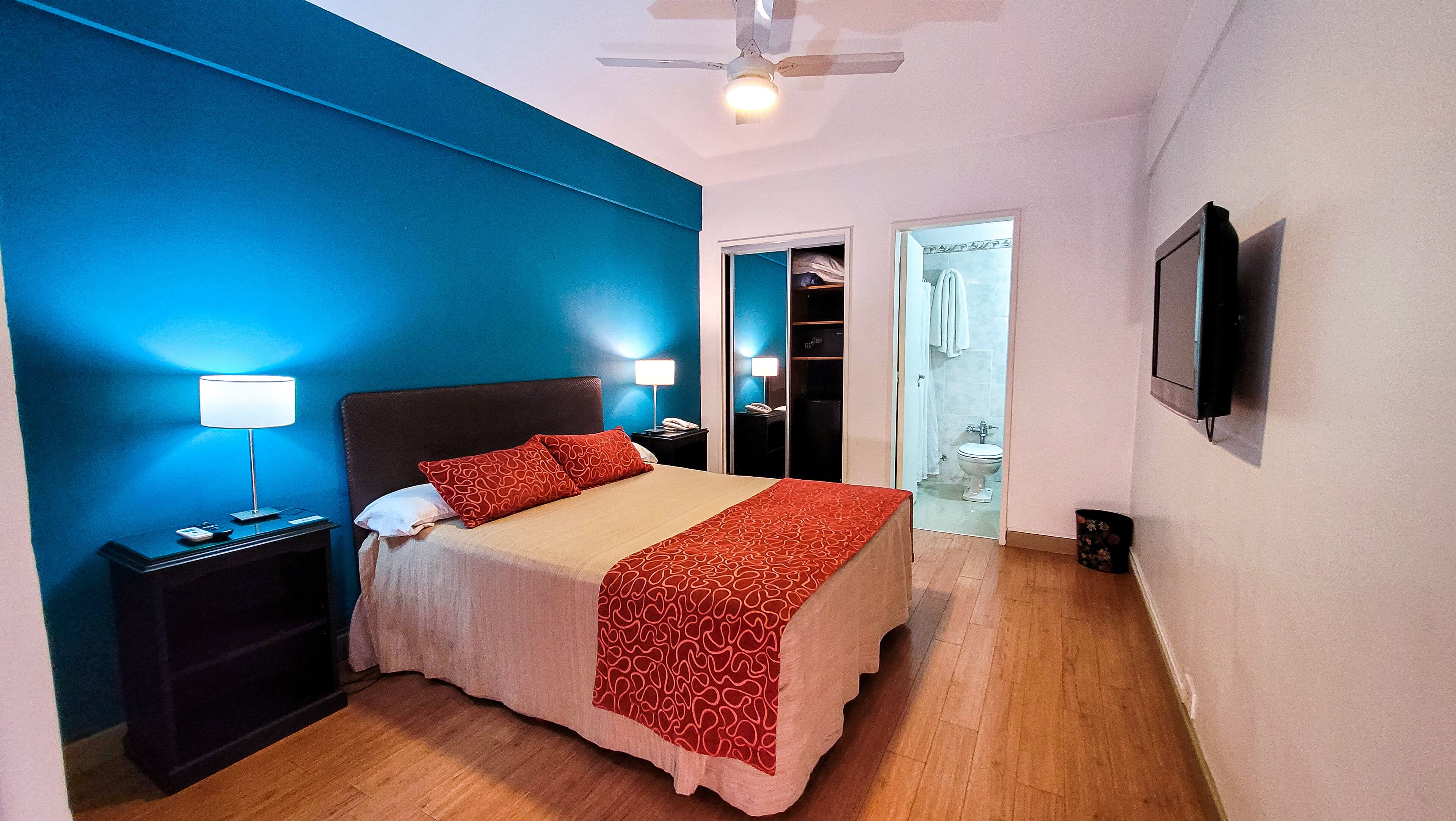 A hotel room with a bed, bedside tables, a ceiling fan, and a bathroom visible through an open door.
