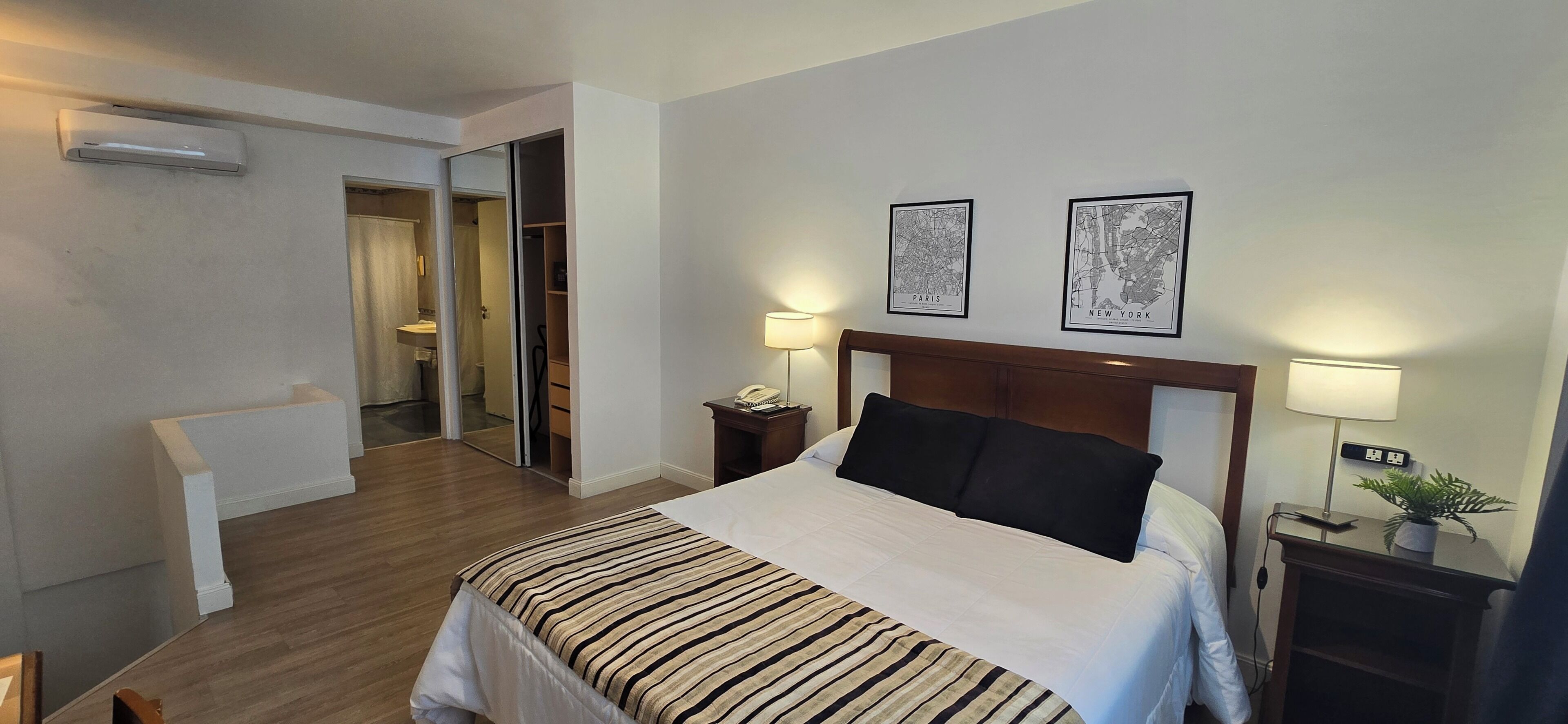 A hotel room with a bed, bedside lamps, a nightstand, a potted plant, and a sliding door leading to a bathroom.