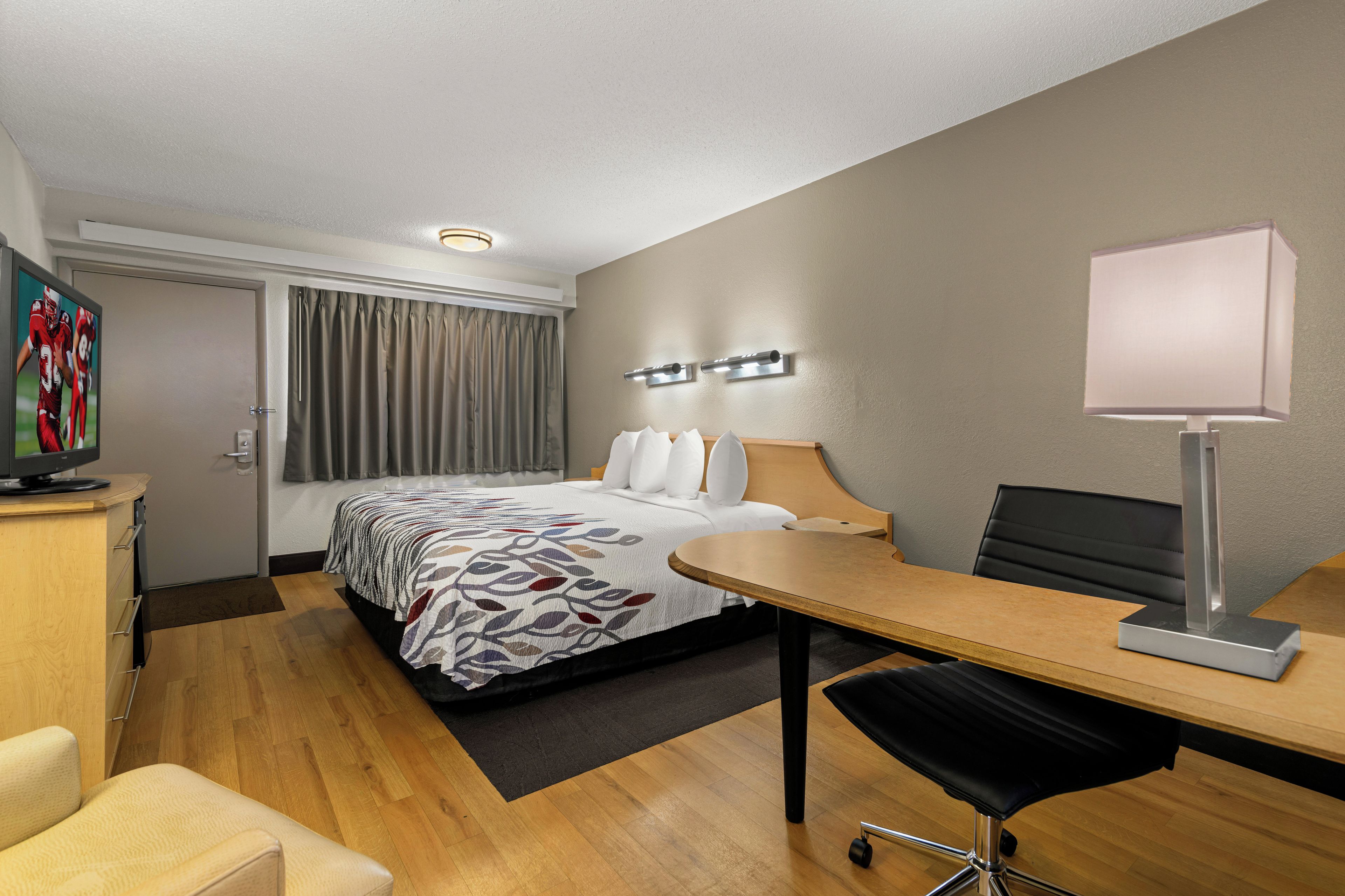 A hotel room with a bed, a desk, a chair, a television, and a lamp.