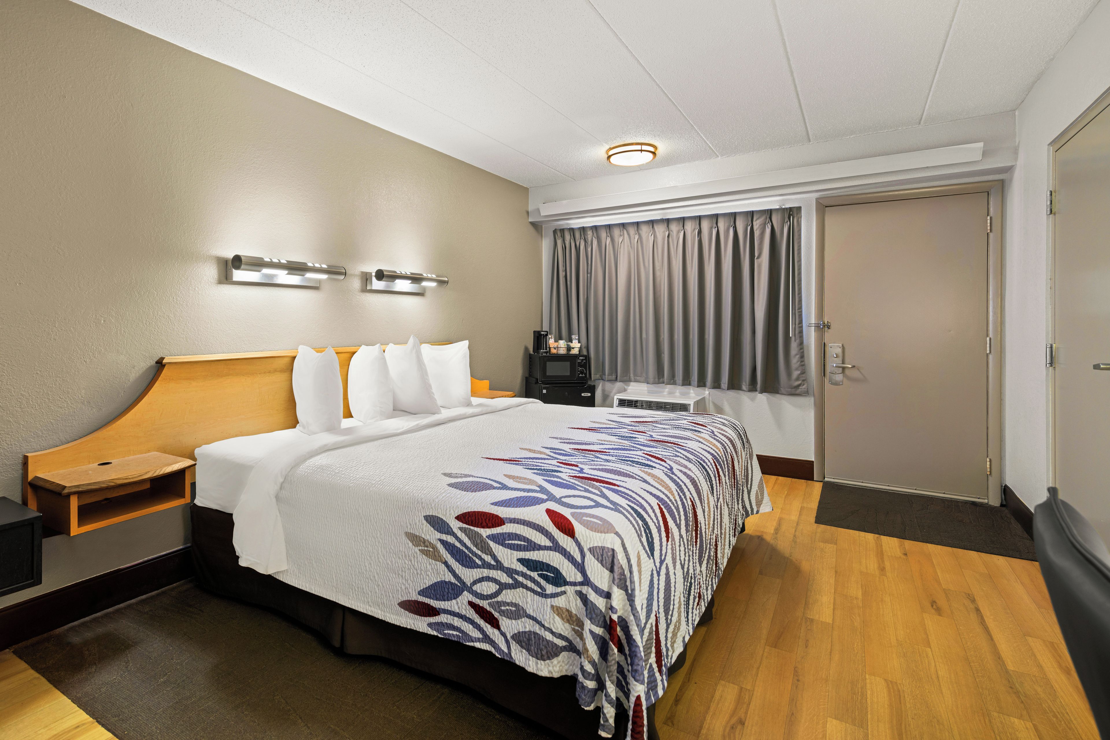 Habitación de hotel con cama, mesitas de noche, escritorio, silla, ventana con cortinas y puerta.