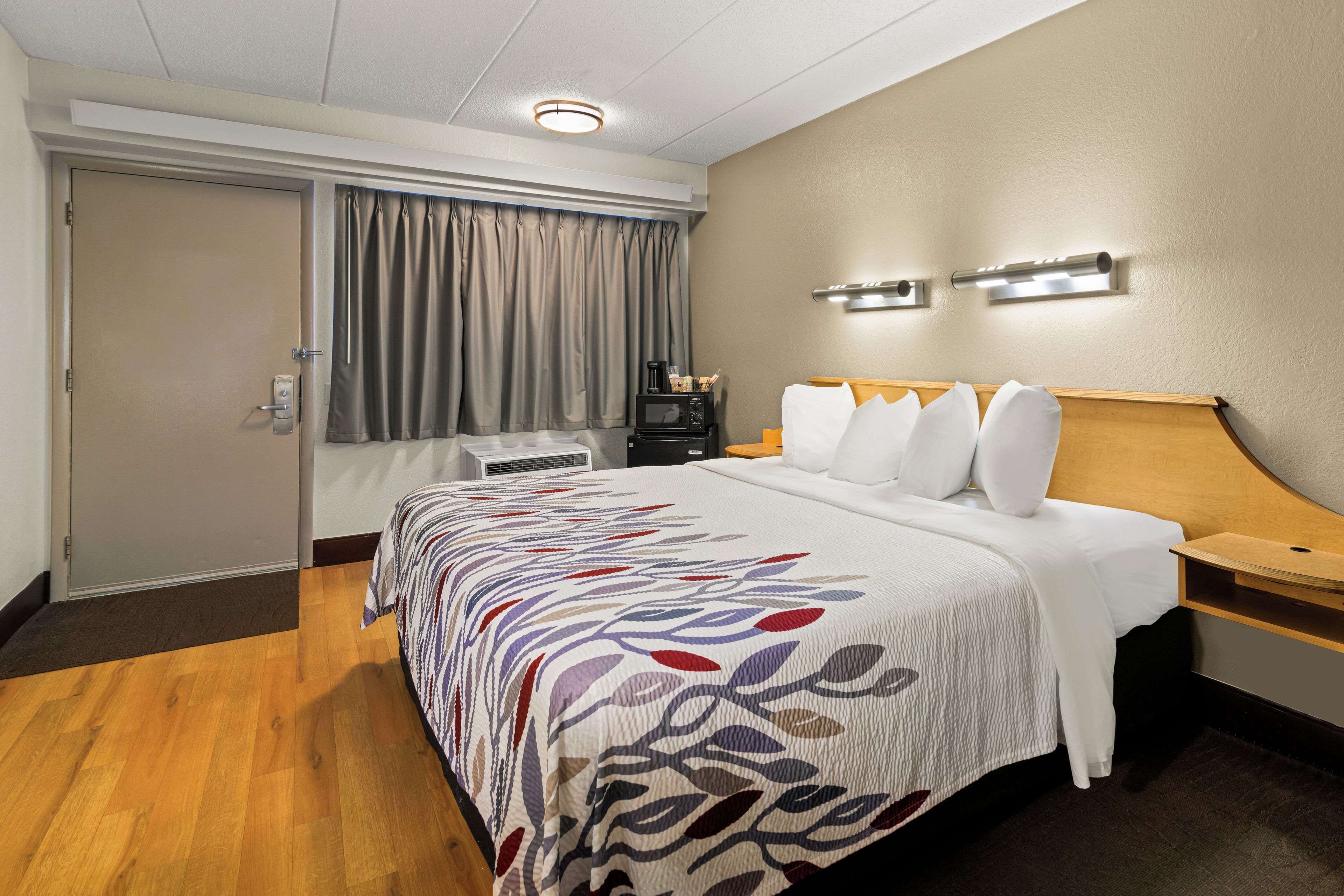 A hotel room with a bed, a desk, a coffee maker, and a window with curtains.