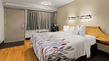 A hotel room with a bed, a desk, a coffee maker, and a window with curtains.
