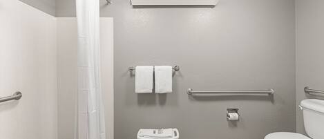 A bathroom with a shower, toilet, grab bars, and a towel rack.