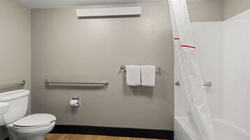 A bathroom with a toilet, a handrail, a towel rack, and a shower curtain.