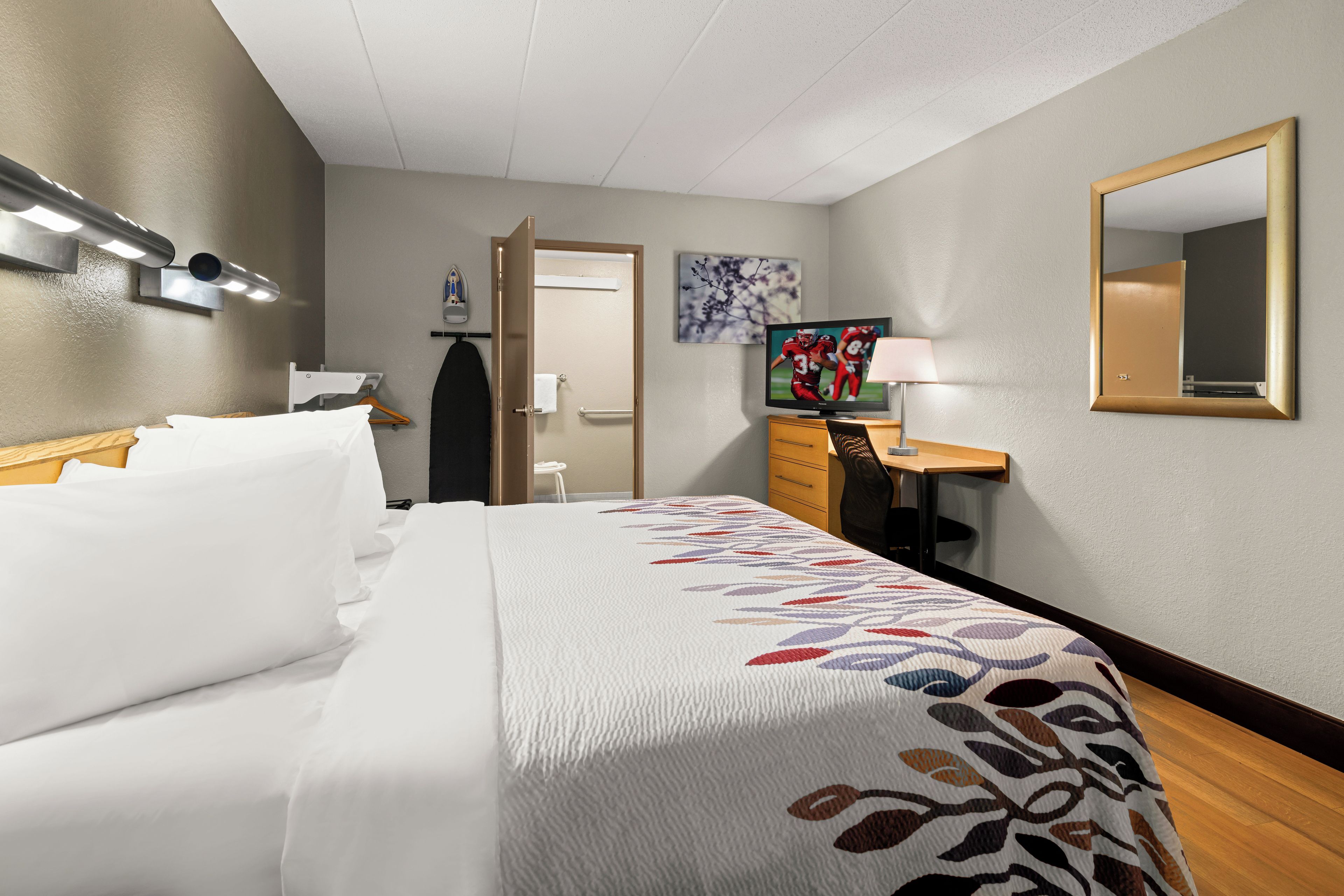 Ein Hotelzimmer mit Bett, Schreibtisch, Fernseher und Spiegel.