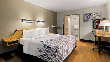 Une chambre d’hôtel comprenant un lit, des tables de chevet, un bureau, une chaise, un téléviseur et un tableau au mur.
