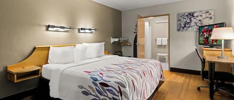 A hotel room with a bed, bedside tables, a desk, a chair, a TV, and a painting on the wall.