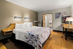 A hotel room with a bed, bedside tables, a desk, a chair, a TV, and a painting on the wall.