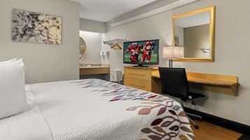Habitación de hotel con cama, escritorio, televisor, espejo y un cuadro en la pared.