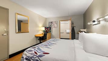 A hotel room with a bed, a desk, a chair, a mirror, a television, and a painting on the wall.