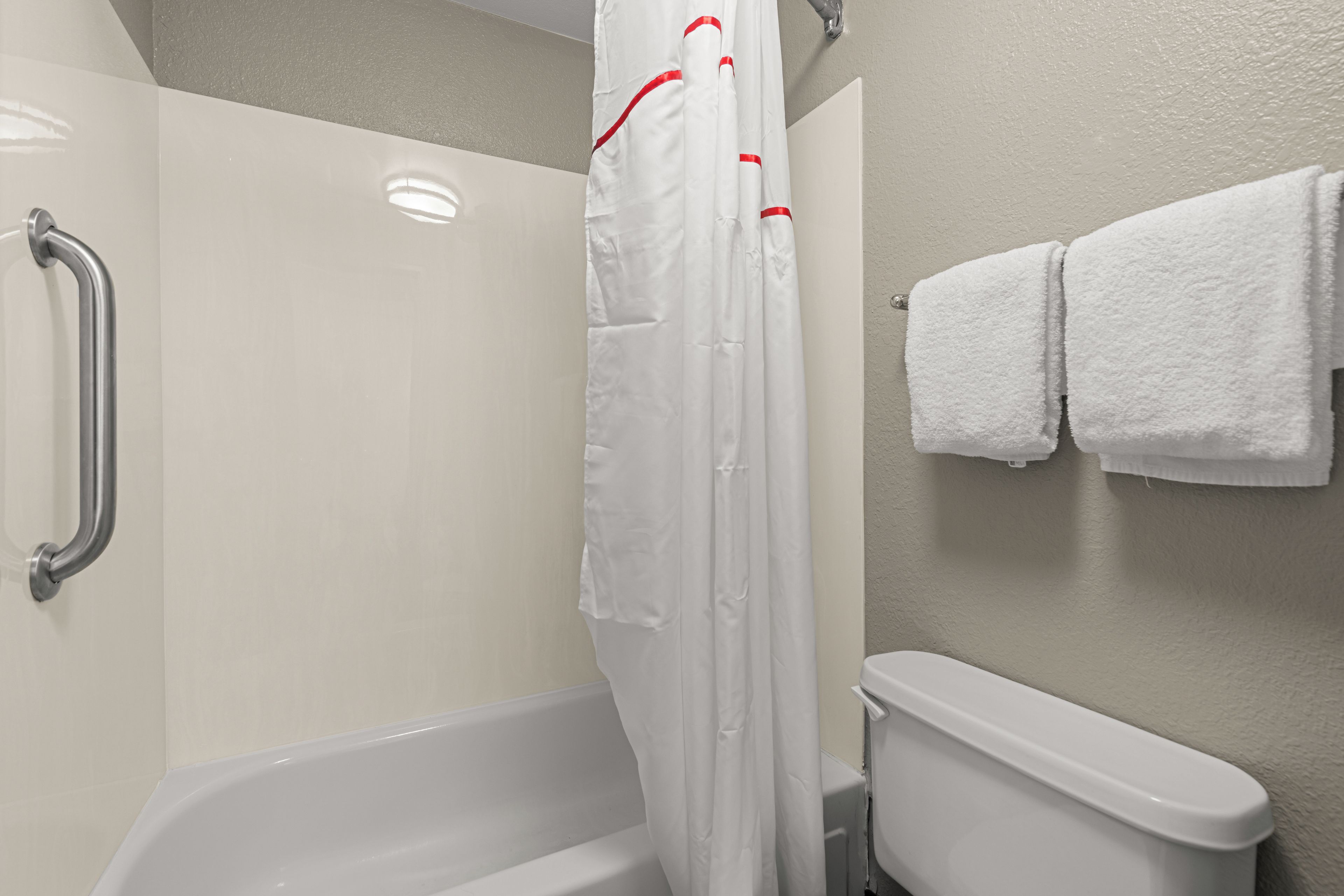 Baño con cortina de ducha, barra de apoyo y un inodoro con dos toallas.