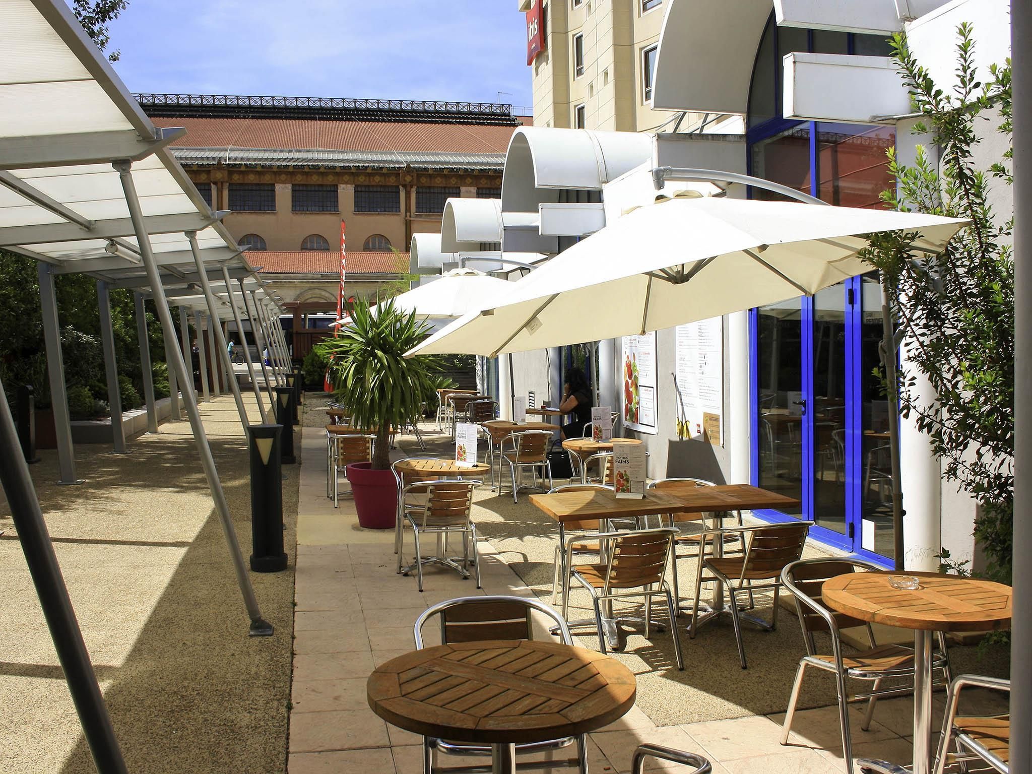 Zona caffè all'aperto con tavoli e sedie, ombrelloni e un edificio sullo sfondo.
