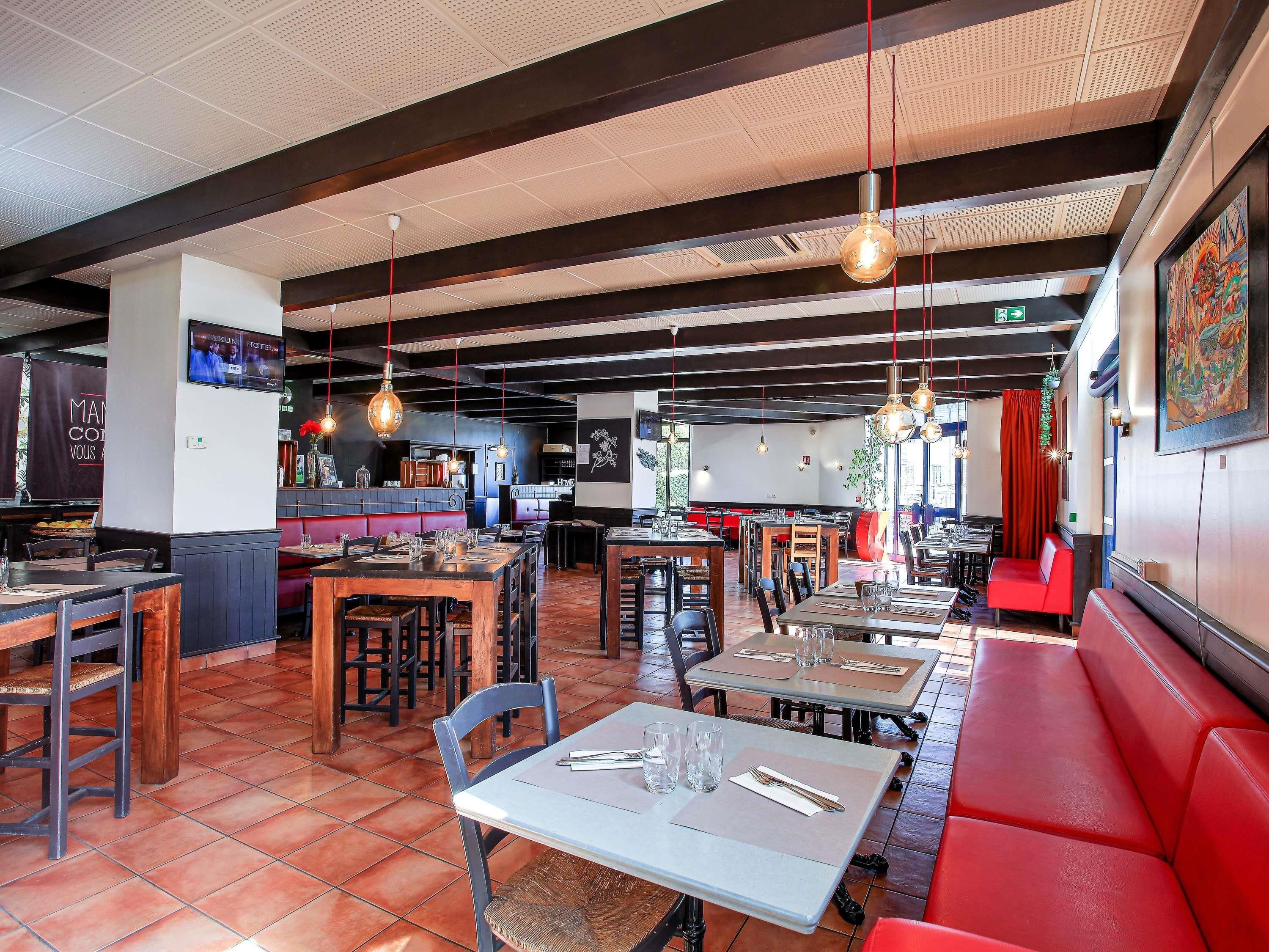 Un restaurante con varias zonas de comedor, incluyendo mesas tipo cabina y mesas tradicionales, un suelo de baldosas y lámparas colgantes.