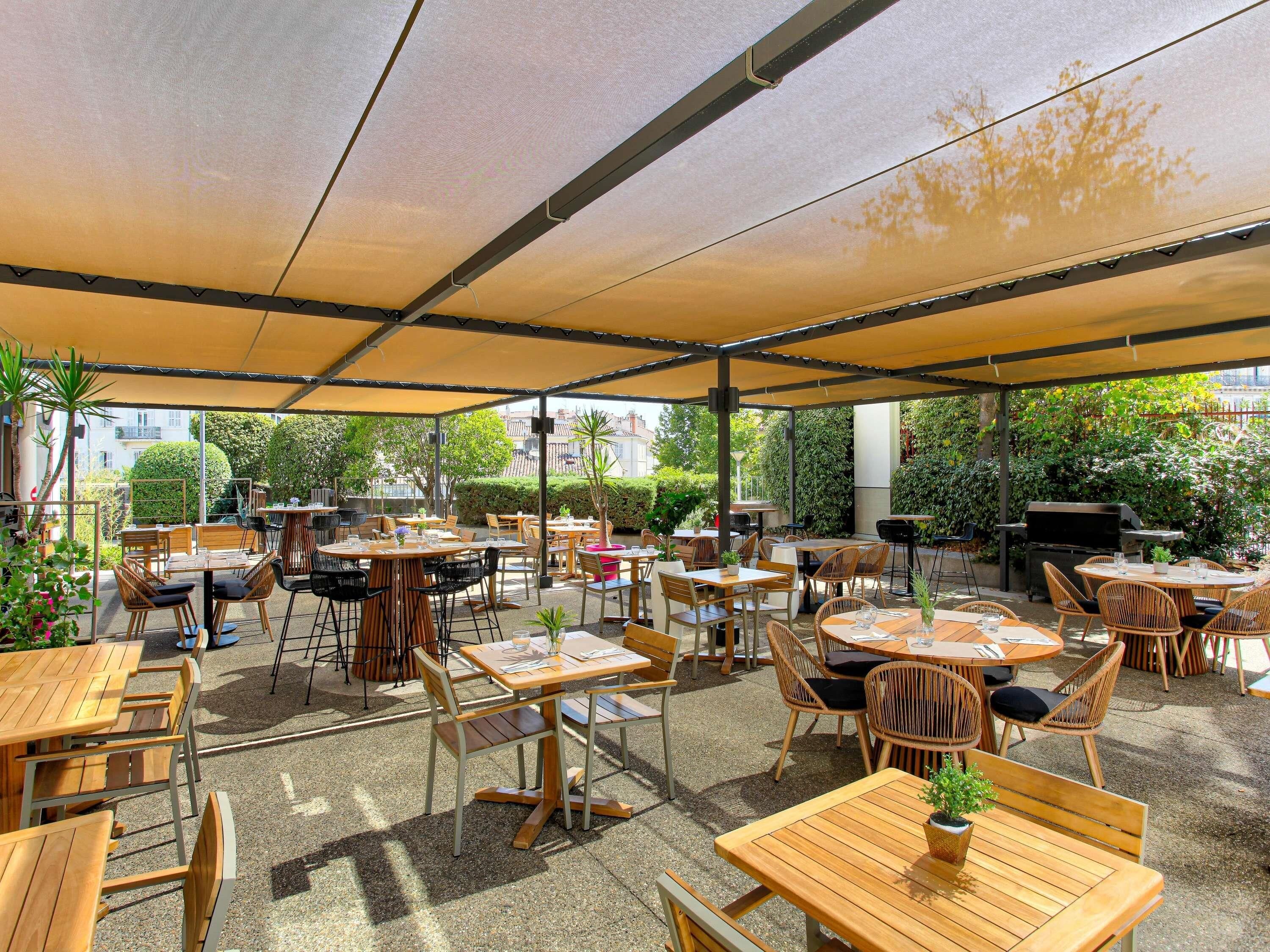 Un patio al aire libre con mesas, sillas, una parrilla y plantas en macetas.