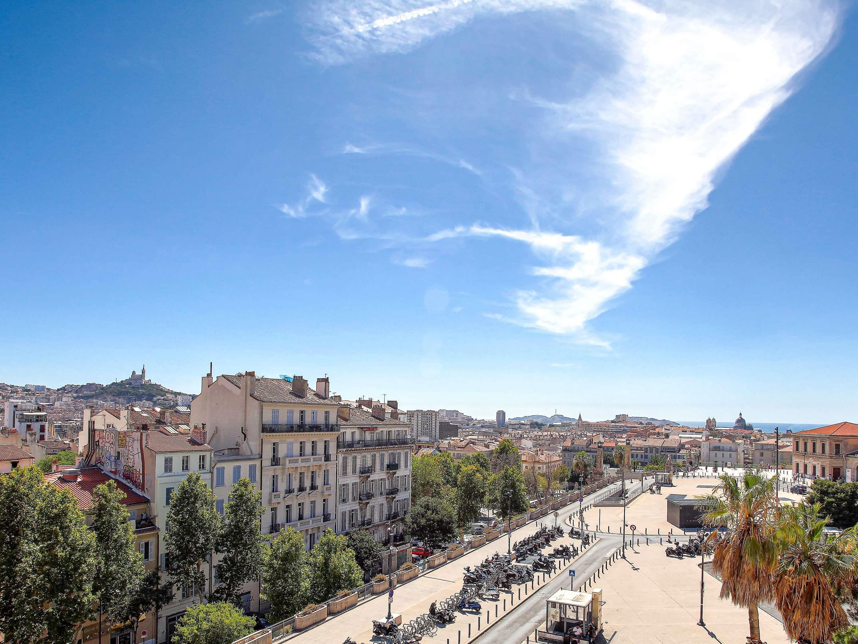 A cityscape with a clear sky, buildings, and a road with parked vehicles.