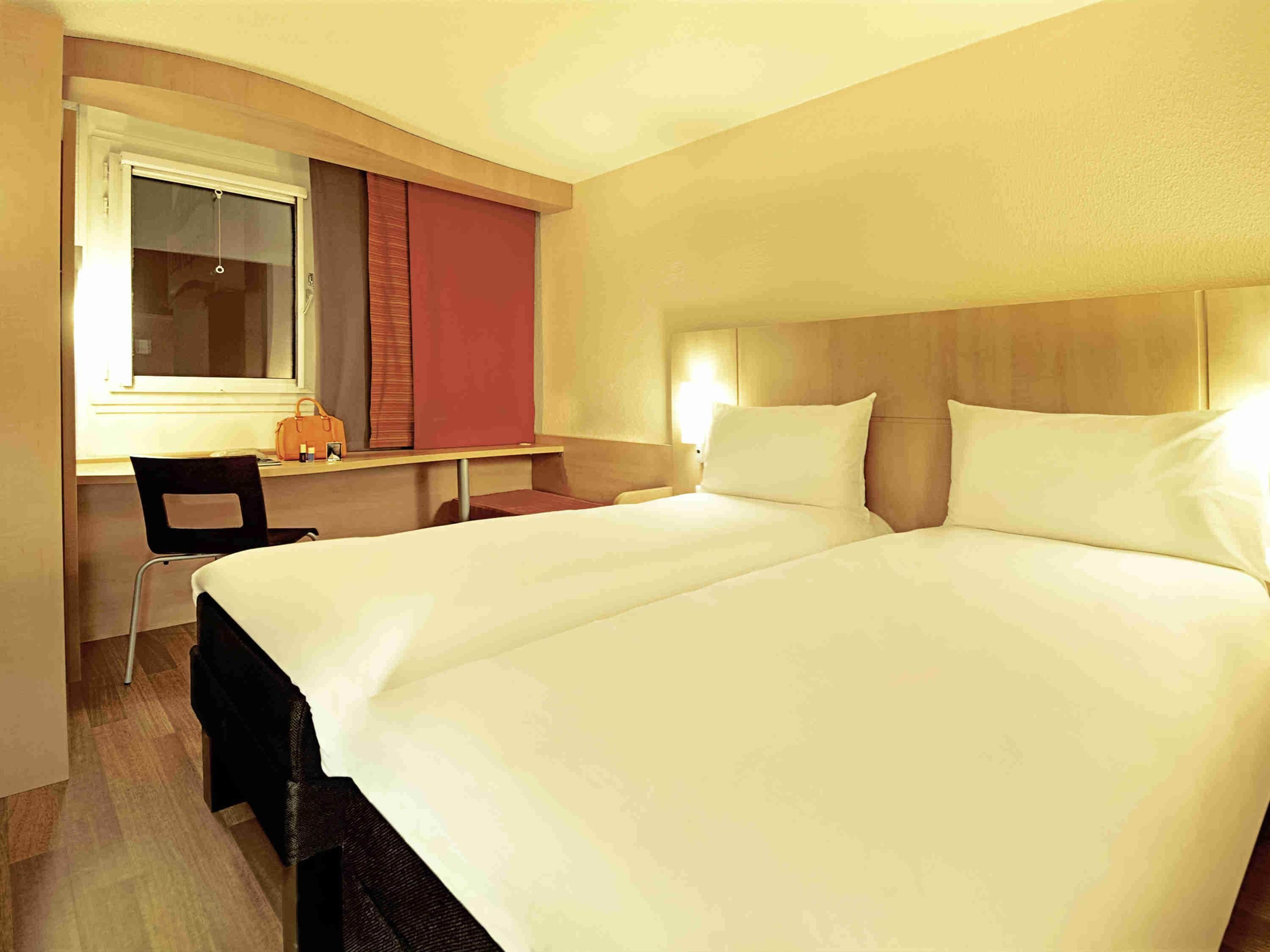 Ein Hotelzimmer mit einem Doppelbett, einem Schreibtisch mit Stuhl und einem fenster mit Vorhängen.