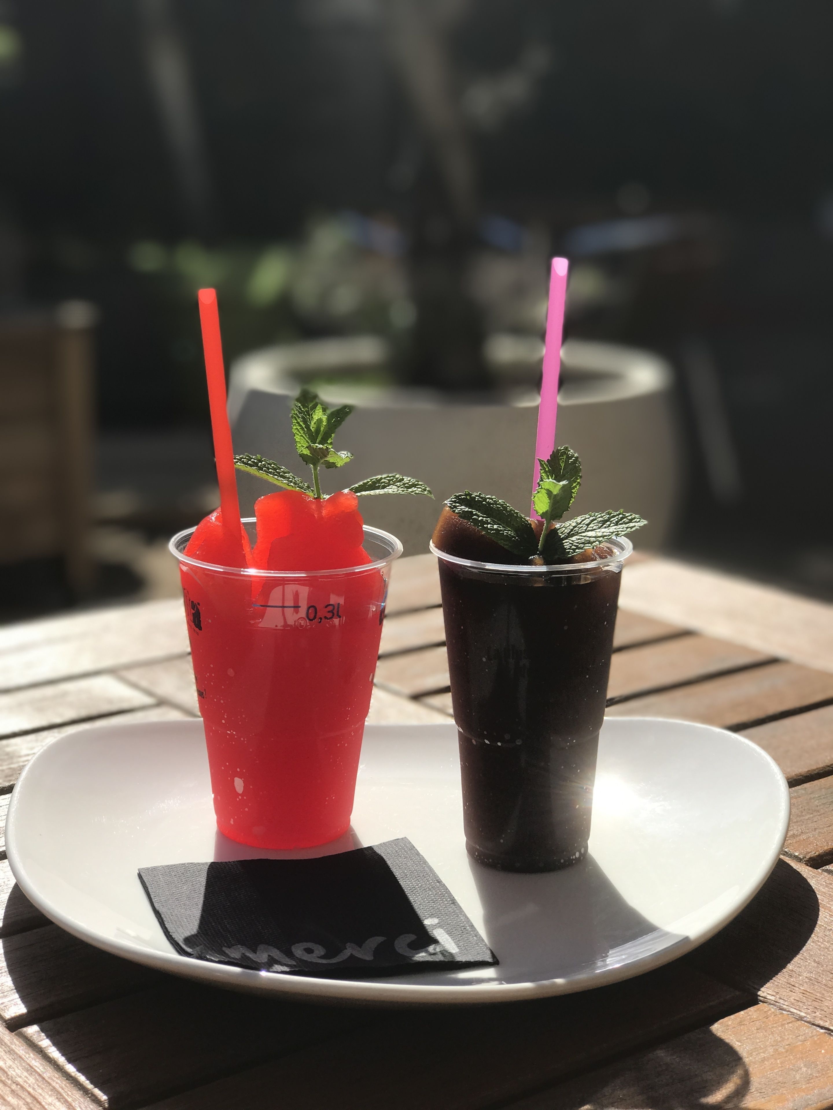 Two plastic cups with straws, one red and one dark, on a white plate with a black napkin.