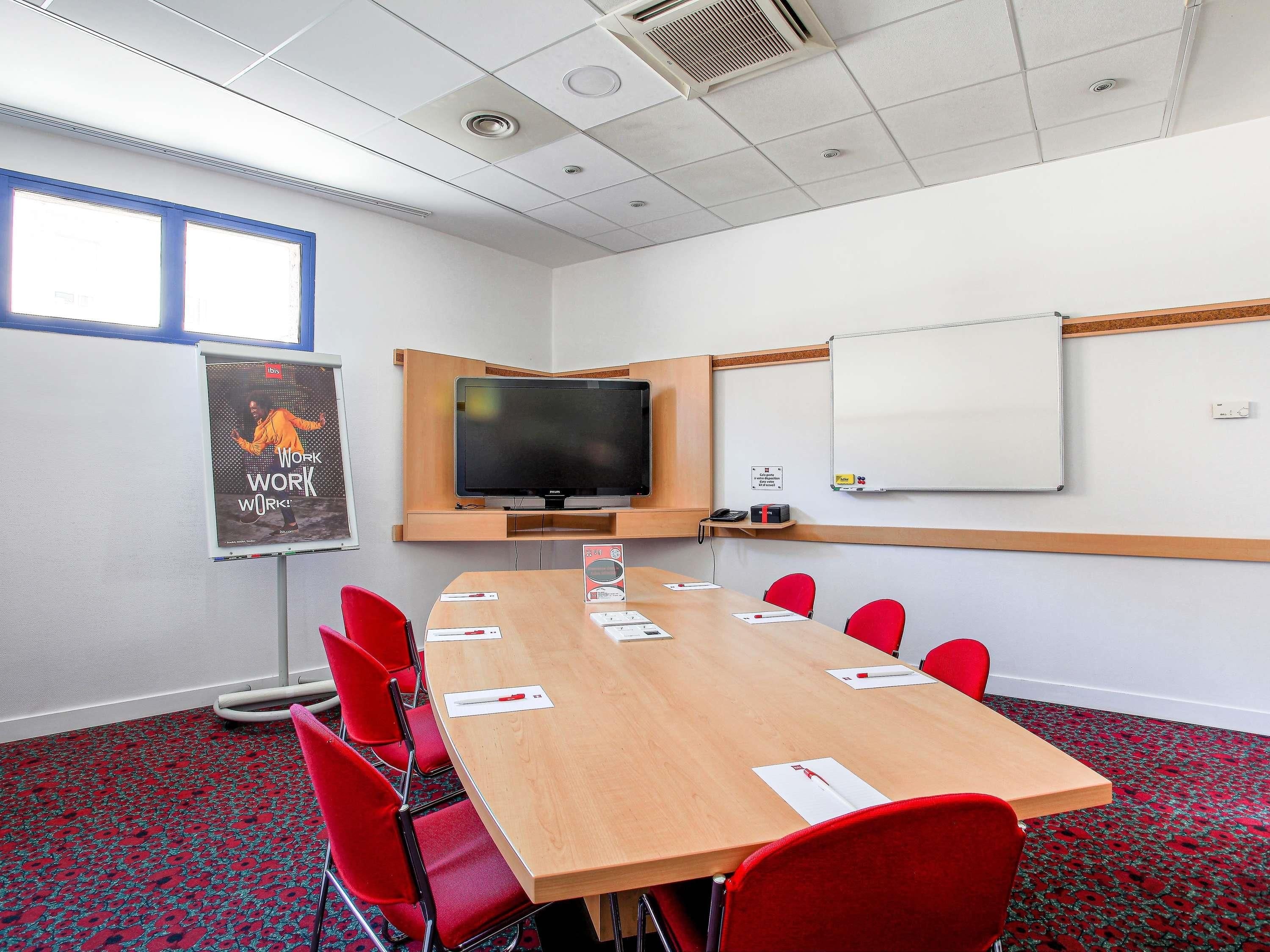 A conference room with a long table, red chairs, a flat-screen TV, a whiteboard, and a poster on the wall.