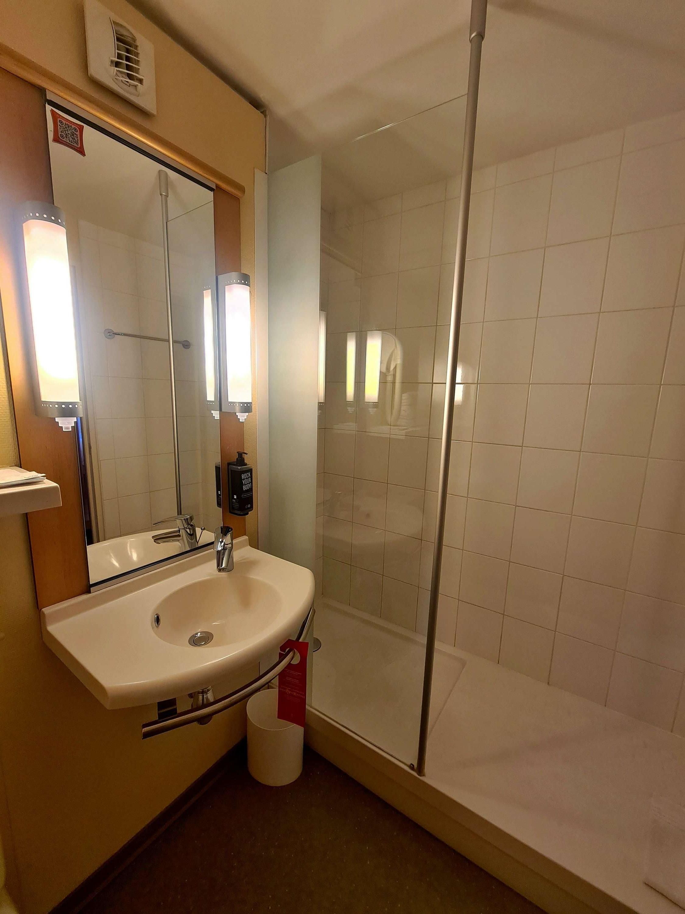 Baño con lavabo, espejo y cabina de ducha con mampara de vidrio.