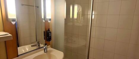 Baño con lavabo, espejo y cabina de ducha con mampara de vidrio.
