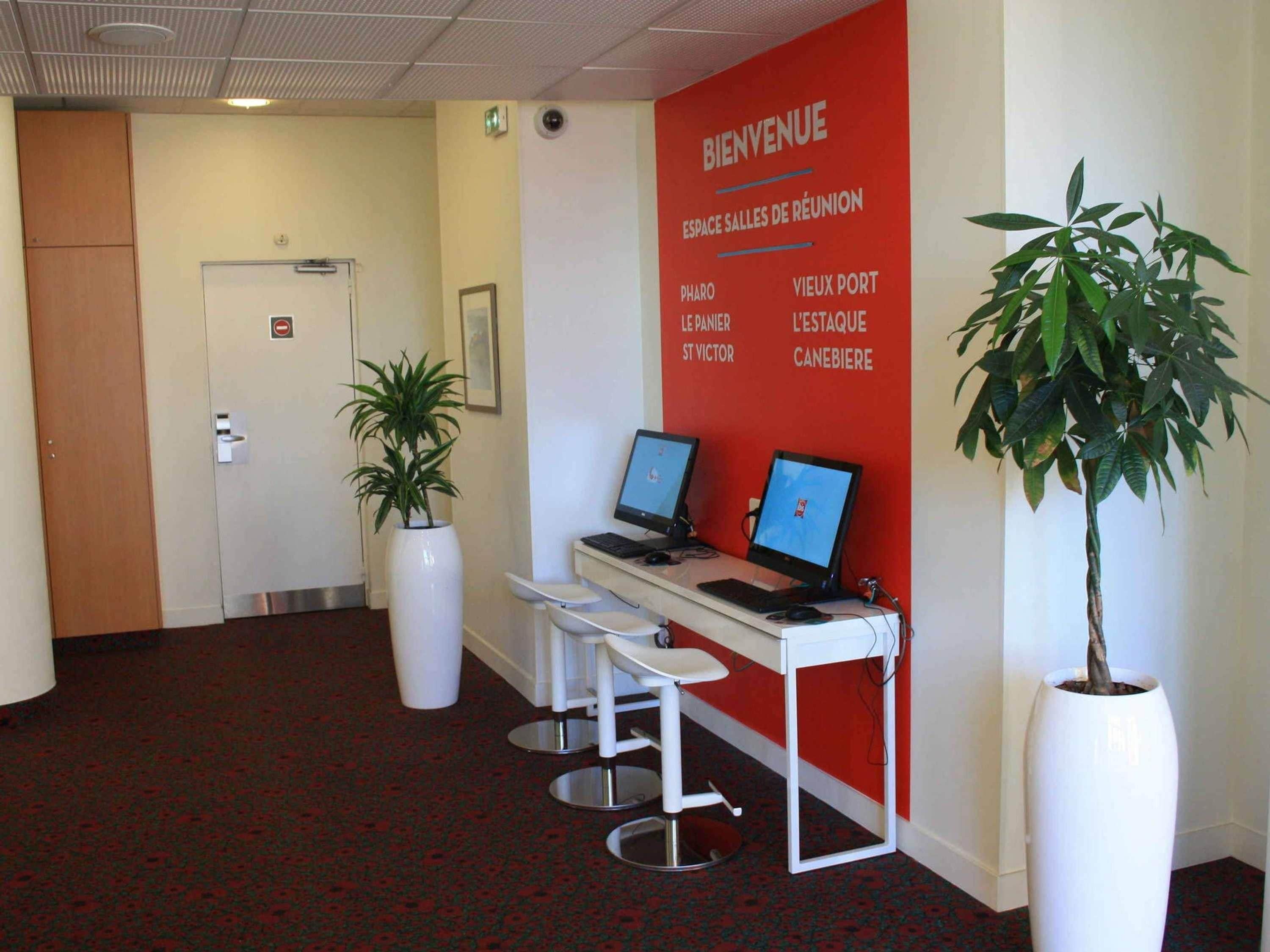 A reception area with a red wall, two computer monitors, a white desk, a potted plant, and a door.