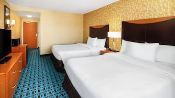 Une chambre d’hôtel avec deux lits, une commode en bois, un téléviseur et une moquette à motifs.