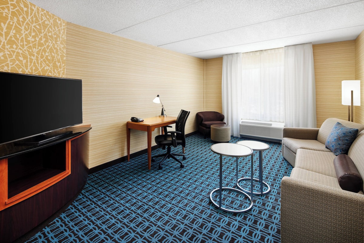A hotel room with a flat-screen TV, a desk with a chair, a sofa, and two small tables.