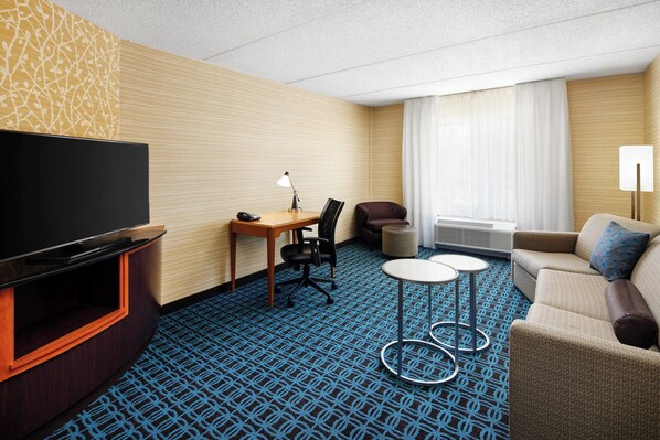A hotel room with a flat-screen TV, a desk with a chair, a sofa, and two small tables. - Fairfield Inn & Suites by Marriott Plainville (Plainville)