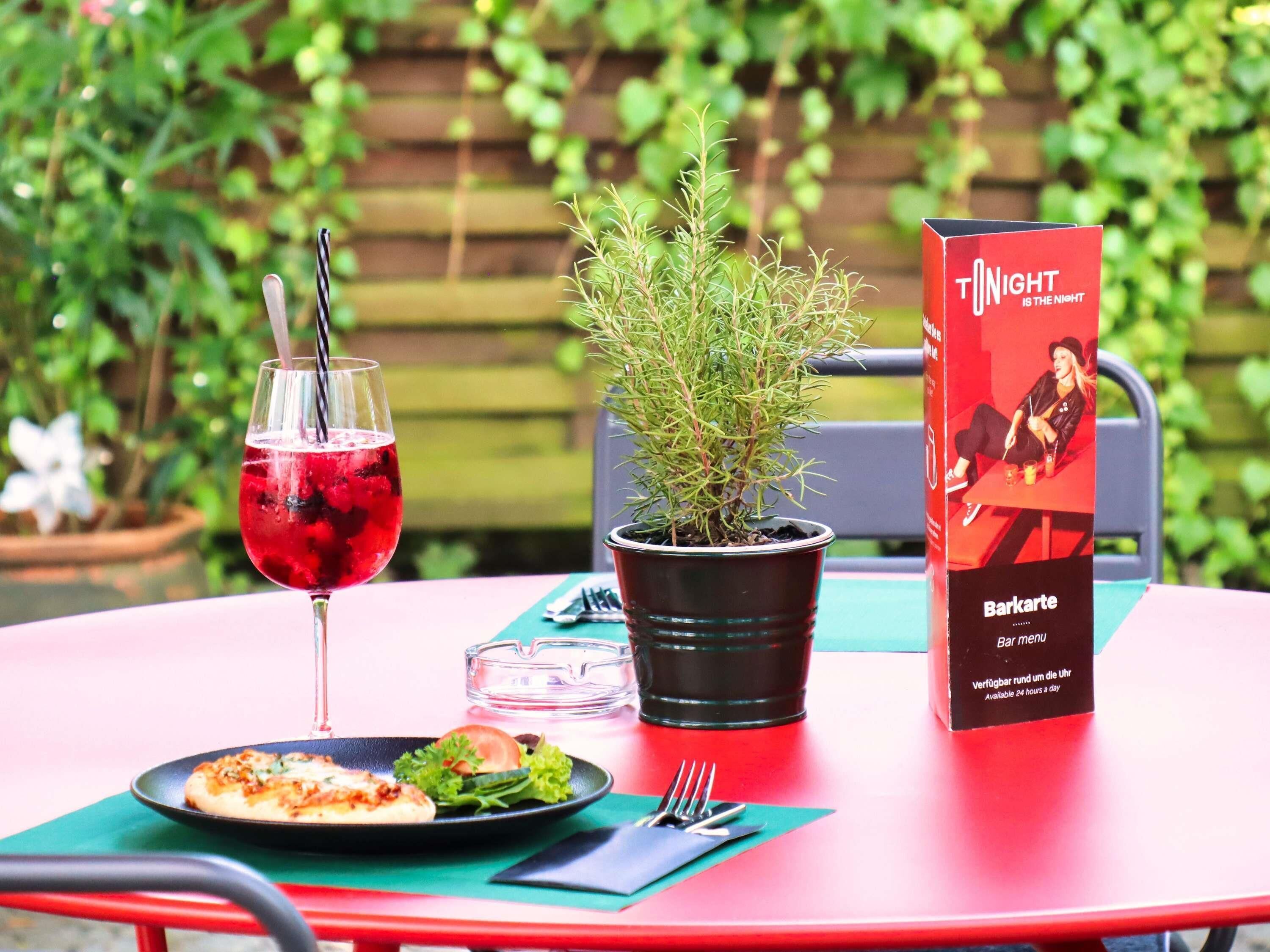 A table with a menu, a glass of red drink, a plate with food, and a potted plant.