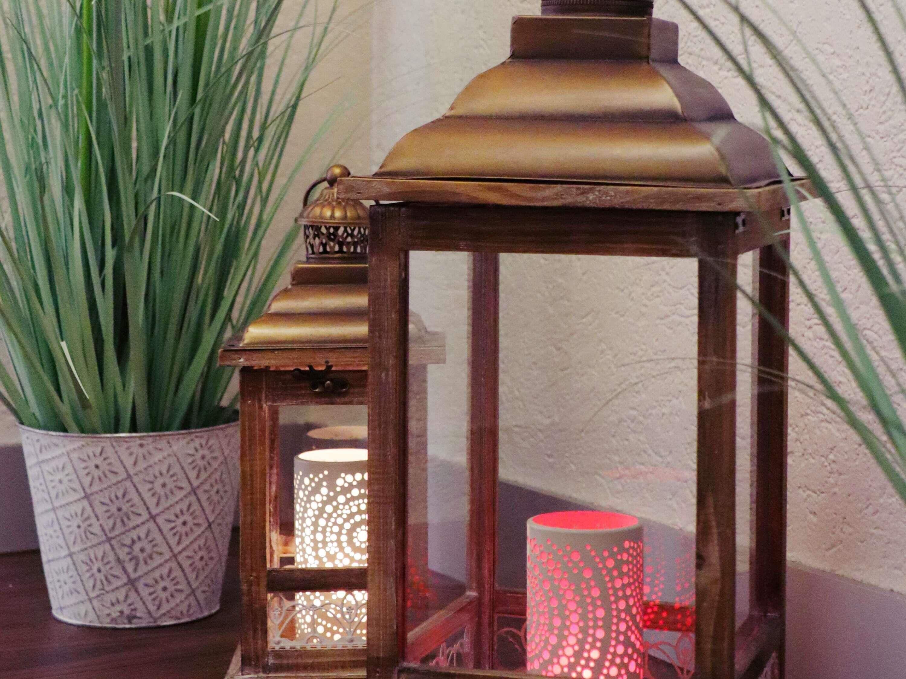 A lantern with a patterned design, a potted plant, and a red cylindrical object.