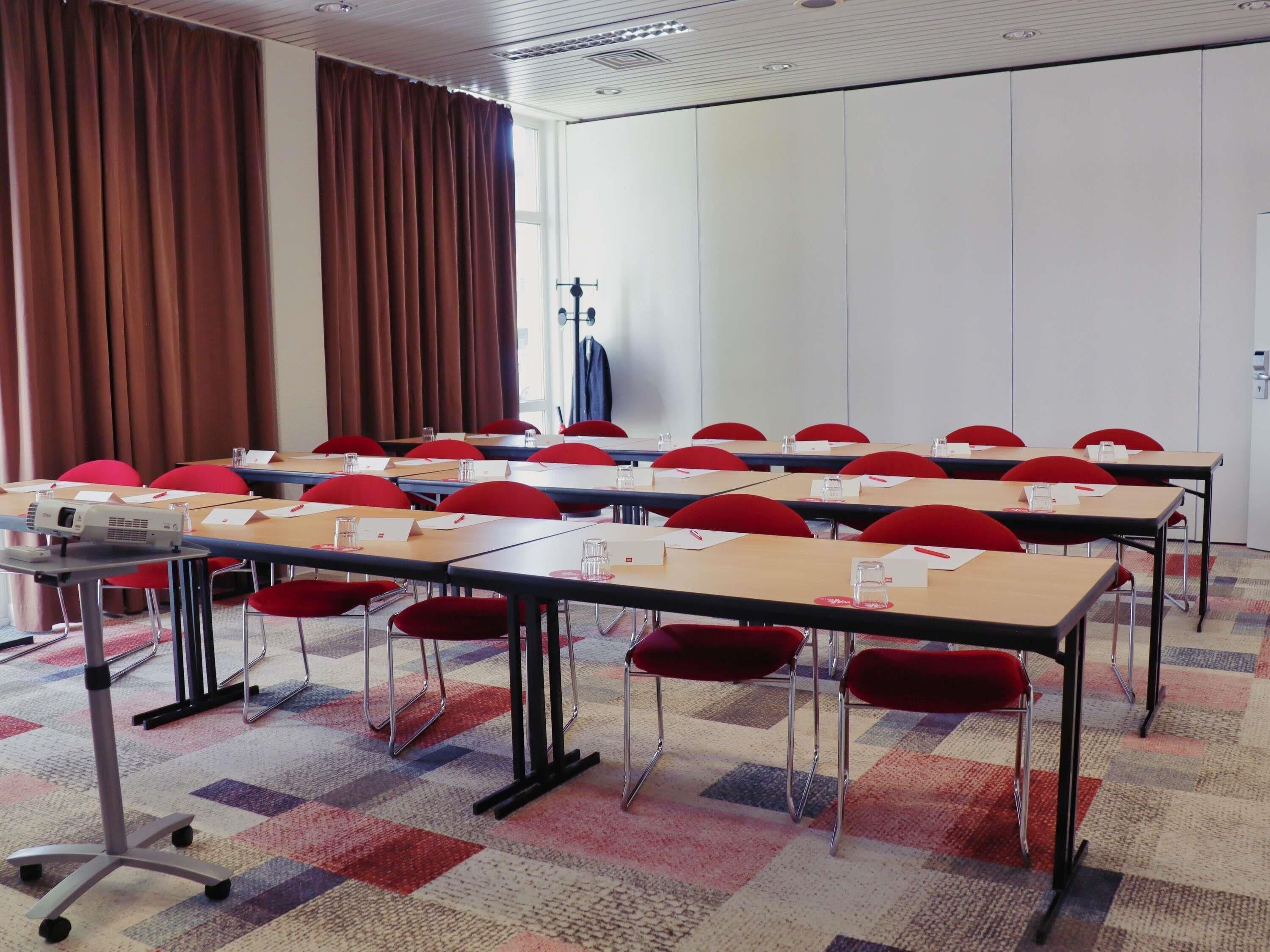 A conference room with tables, chairs, a projector, and a large window with curtains.