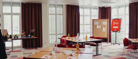 Un salón de conferencias con mesas, sillas, una pizarra y un amplio ventanal con cortinas.