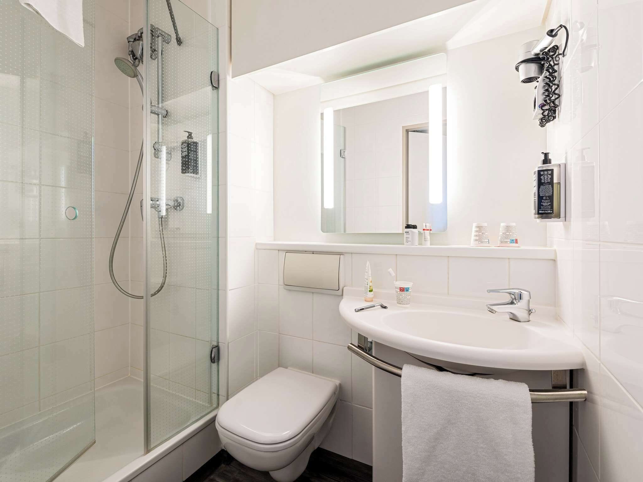Un baño moderno con ducha de vidrio, inodoro blanco, lavamanos con toallero y espejo.